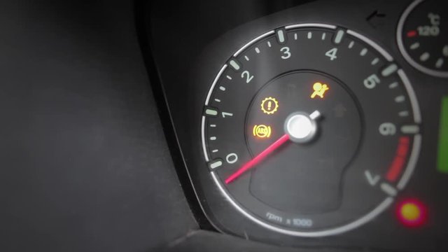 Color footage with various icons lighting up on a car's dashboard, with engine starting.