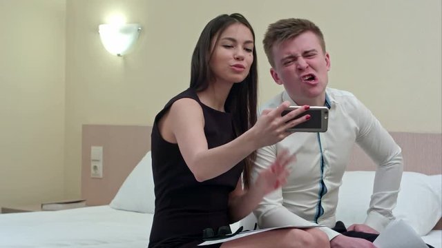 Couple having fun taking selfie sitting on bed in the hotel room
