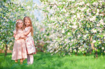 Adorable little girls on spring day outdoors walk in apple garden
