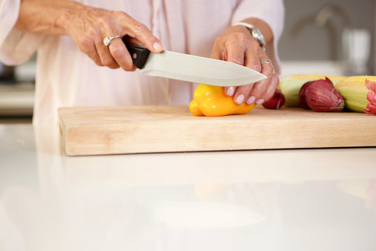 older woman cutting fresh vegetables in kitchen