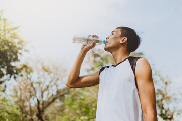 Sports man drinking water after exercising on background of green trees.