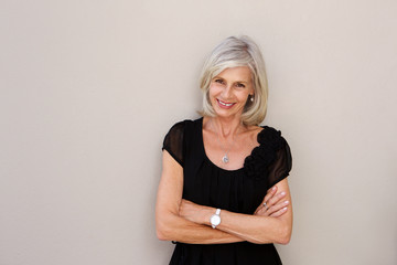 smiling older woman leaning on wall with arms crossed