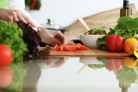 Closeup of human female hands cooking vegetables salad in kitchen on the glass table with reflection. Healthy meal and vegetarian concept