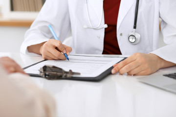 Close up of a female doctor filling up  an application form while sitting at the table. Medicine and health care concept