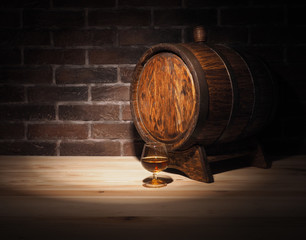 Glass of cognac with barrel on wooden table