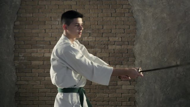 A young karateka practices oriental martial arts and katana usage  in studio