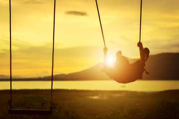 Child enjoying the swing outdoors with river and mountain view on sunset time
