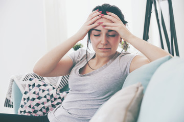 Young worried woman with headache while sitting on comfortable sofa