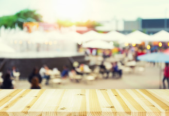 Blurred image of food fairs and food festivals consist of many booth and vendors at food stalls. People walking in street. Event in Chiang Mai at twilight montage with wood table top for background.