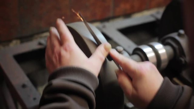Close up footage of a man's hands sharpening a scissors.