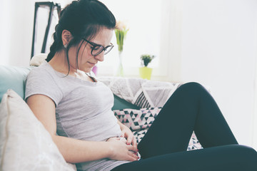 Young woman in pain while sitting on comfortable sofa, home