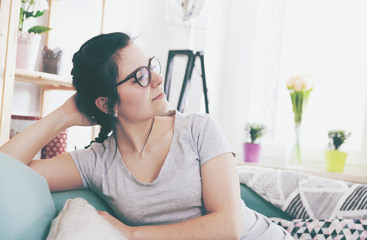 Young relaxed woman smiling while sitting on comfortable sofa, home