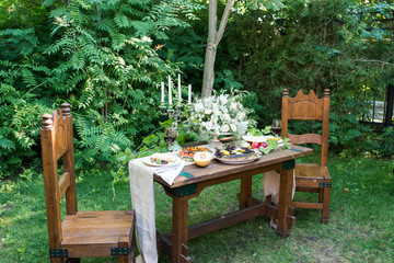 Wedding wooden banquet table. Wooden retro chair. Served table with a glass of red wine, melon, red currants, gooseberry, grilled vegetables