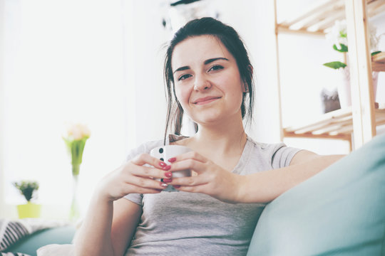 Young relaxed woman drinking coffee while sitting on comfortable sofa