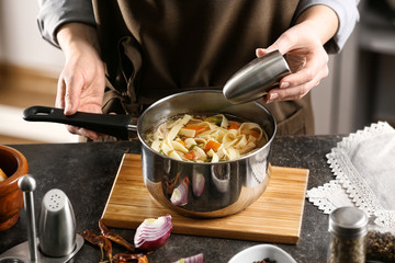 Woman cooking chicken noodle soup at kitchen table