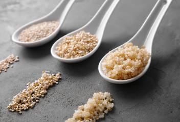 Three ceramic spoons with organic white quinoa grains on dark background