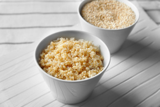 Two white bowls with sprouted organic quinoa grains on white wooden board