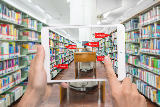 computer in a libAugmented reality education concept. Hand holding digital tablet smart phone use AR application to check library category 