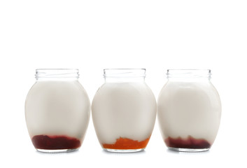 Glass jars with tasty yogurt and jam on white background