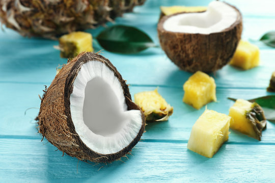 Half of fresh coconut and pineapple pieces on color wooden background