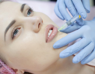 Obraz na płótnie Canvas Hands of cosmetologist making injection in face, lips. Young woman gets beauty facial injections in salon. Face aging, rejuvenation and hydration procedures. Aesthetic cosmetology. Close up.