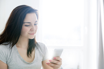Young woman using mobile phone while sitting on comfortable sofa at home