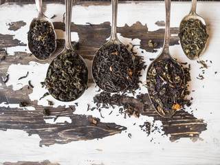 Various dry tea in spoons and scattered on the  old wood  surface
