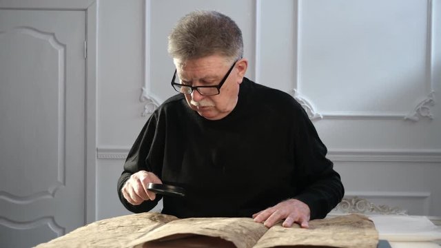 A senior man explores some ancient Torah or Talmud manuscript with a head lens
