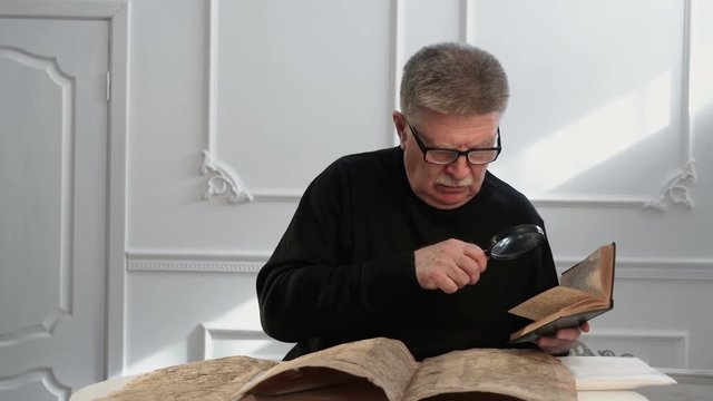 A senior man explores some ancient manuscript and uses an old book and a hand le