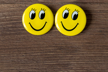 Two yellow buttons with smiley faces on a wooden background. Close up