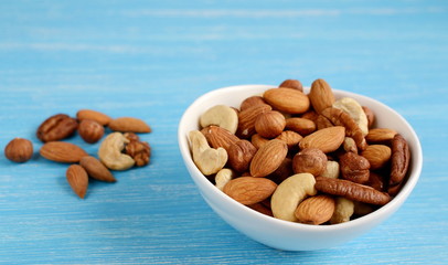 White bowl of nuts, almonds, walnuts, pistachios, cashew, hazelnuts. Blue wooden background