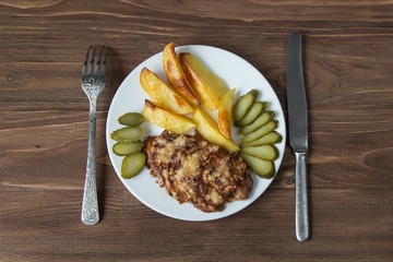 Grilled meat with potato and cucumbers on a wooden background