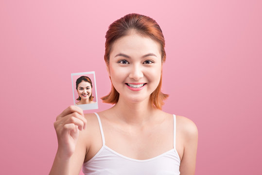 Young asian woman holding her polaroid picture on pink background.