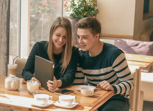 Cheerful couple dating in a cafe. They are having fun and smiling with tablet.  Dating, love, romanic, dating, lifestyle, study, education.