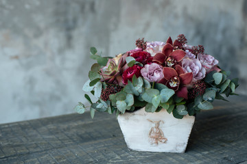 A bouquet of roses in a wooden vase is on the table. Flower arrangement in a wooden flowerpot