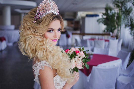 Young fashion bride with perfect skin and make up, curly hair, flowers and tiara on the head, indoors