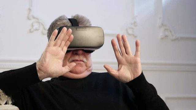 A grey headed man keeps a head-mounted display on his head and watches images of