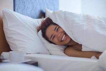 Obraz na płótnie Canvas Young happy black woman lying in a bed.