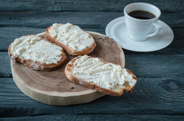 Breakfast with homemade sandwiches with cream-cheese on a black wooden table. Wooden stand with sandwiches.