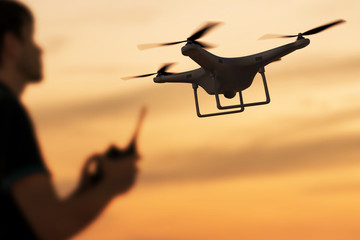 Man is controlling flying drone at sunset. 3D rendered illustration of drone. - obrazy, fototapety, plakaty