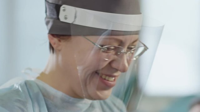 Tilt down of middle aged nurse in medical face shield smiling and holding test tube