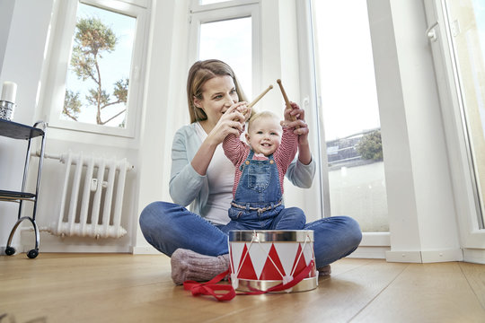 Mother and baby girl sitting on floor playing drums