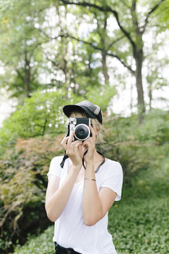 Young woman with a vintage camera taking pictures in park
