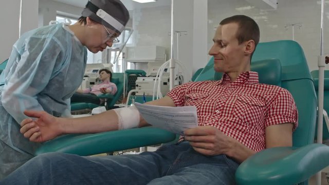 Woman giving blood bank donor agreement to man and explaining him something after procedure of blood drawing