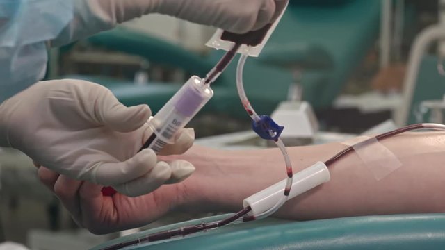 Closeup shot of hands of nurse taking blood from arm donor to test tube. Man squeezing stress ball during procedure of drawing venous blood 