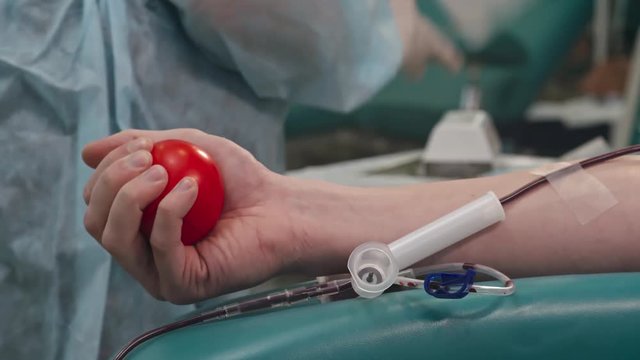 Tracking shot of male donor squeezing stress ball during procedure of drawing blood at donation station