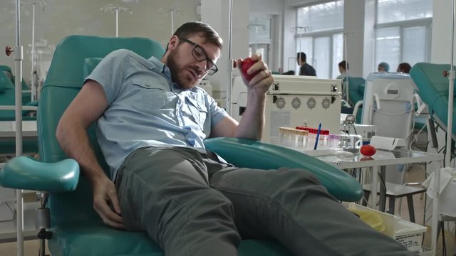 Young man sitting in medical chair in hospital and holding stress ball before blood donation