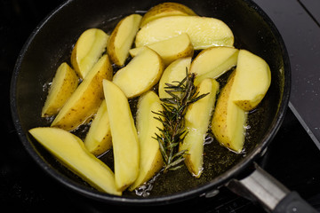 Potato slices fried in oil in a frying pan with rosemary