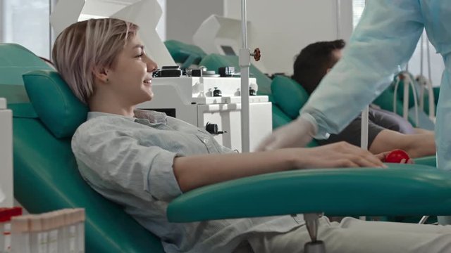 Young woman smiling and talking to doctor tapping vein on her arm and reading blood donor agreement before obtaining blood