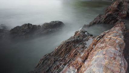 Long Exposure with smooth surface of water near a beach with full of beautiful rocks